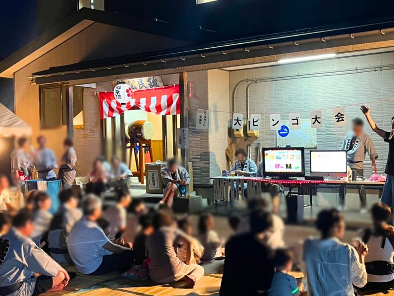 公民館前で開かれた大ビンゴ大会。モニターの前にシートを敷いて座る大勢の参加者