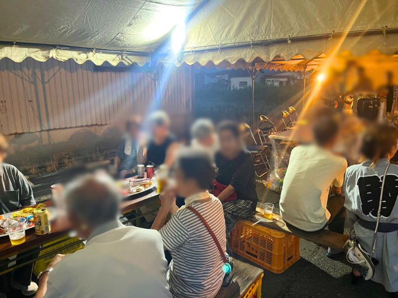 テントの下、長机を囲んで談笑する才津1丁目夏まつりのビアガーデンの参加者