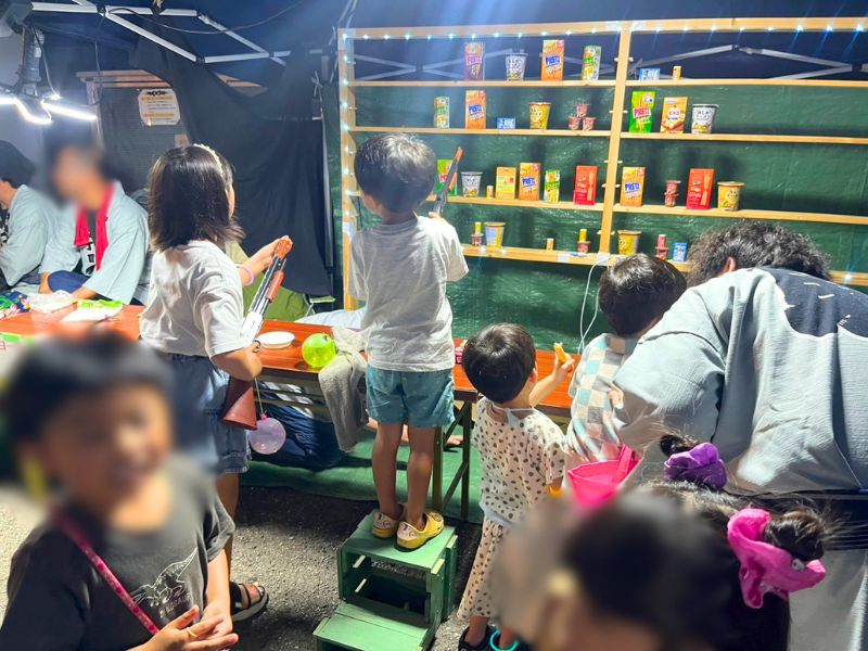 棚に並んだお菓子をコルク銃で狙う子どもたち。射的コーナー
