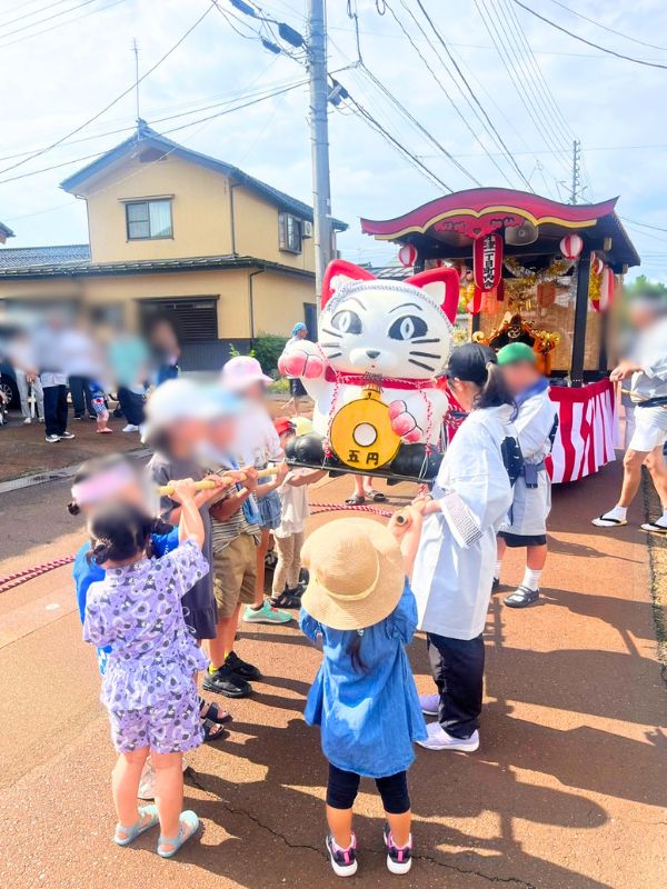 招き猫を載せた子ども神輿と、お囃子の笛を吹く子どもたち